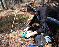 Student placing soundscape equipment by river to receive sound data.
